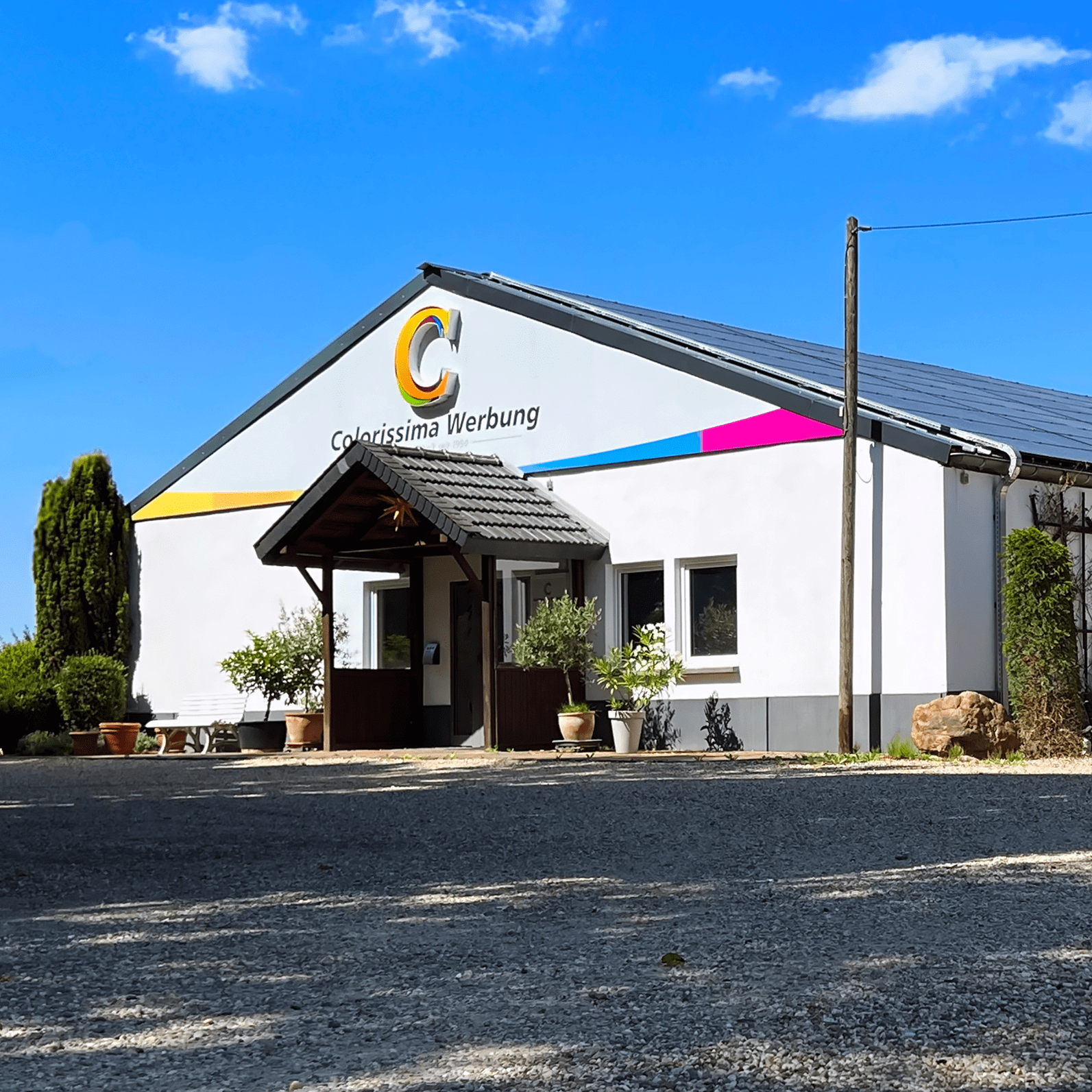 Kontaktieren Sie uns! Das Gebäude von Colorissima Werbung, bei wolkenklarem Himmel. Es ist eine große und lange Halle.